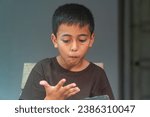 Small photo of A boy loves a cell phone while eating popcorn with gusto. Boy staring at cell phone while eating popcorn. The boy happily sat and ate popcorn.