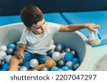 Small photo of Toddler boy playing with a toy while sitting in a ball pit full of colorful balls. A ball pit - a great place for kids to jump, crash, and wiggle. Sensory play at the nursery school. . High quality