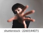 Short-haired young woman reaching towards the camera. Blurred hand in the foreground. Focus on the background. High quality photo