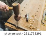 Small photo of carpenter working on wood by using a mallet and a chisel, workshop, other tools on the wall. High quality photo