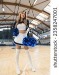 Small photo of Cheerleader woman in a black and white uniform with blue pom pons standing on a basketball court . High quality photo