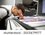 Small photo of Worker checking print quality of graphics in modern printing house.