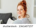 Small photo of Smiling friendly young redhead woman looking at the camera with an impish grin as she relaxes at home on a sofa