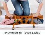 Midsection of young woman packing suitcase on bed