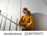 Young serious girl with folded arms stands in front of metal wall and looks to the side