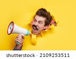 Small photo of Mad funny male with mustache screaming in loudspeaker and announcing news while looking through torn yellow paper background in studio