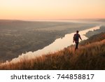 Anonymous backpack walking on top of hill with view of river and terrain on background. 