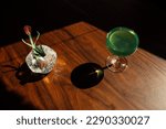 paper tulip in vase with green absinthe drink, cocktail on wooden table in the sun with harsh shadows