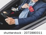 Small photo of Parliamentary immunity concept. Man in blue suit shows red ID card or pass. An important untouchable employee of ministry is driving a car. state Duma deputy of Russia inscription on the red document.
