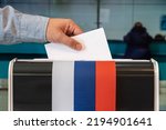 Small photo of man putting electoral billuten in a box during elections in russia. russia flag. voters to vote on a single voting day in Russia at a polling station