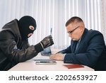Small photo of businessman and robbers are sitting at a table. A racketeer in a black balaclava forces to sign a contract. The concept of a raider takeover of the company. dangerous deal