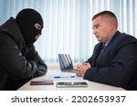 Small photo of businessman and robbers are sitting at a table. A racketeer in a black balaclava forces to sign a contract. The concept of a raider takeover of the company. signing of important documents.