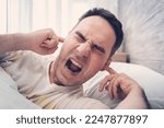 Small photo of the young man is irritated by extraneous noises during sleep. Noisy neighbors or repairs interfere with rest. The concept of noise.
