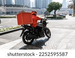 Small photo of A food delivery courier is driving an order to a customer's home on a moped. takeaway food during quarantine. transport delivery of parcels at home. motorcycle rider with big backpack