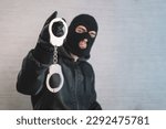 Small photo of a bandit in a black mask and gloves with handcuffs in his hands on a white background. Release from imprisonment. Prison break concept. Jailbreak