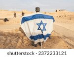 Back view of Israeli soldier with white and blue flag of Israel against the background of the desert and rocks.. Military men protecting promissed land. National flag of Israel. War conflict