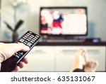 Men with the remote control front of the television. Hand with remote control directed on the TV. A man is relaxing and watching sports on TV.