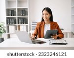 Successful Asian Businesswoman Analyzing Finance on Tablet and Laptop at modern Office Desk tax, report, accounting, statistics, and analytical research concept