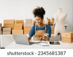 Startup small business SME, Entrepreneur owner African woman using smartphone or tablet taking receive and checking online purchase shopping order to preparing pack product box. 