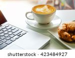 coffe, laptop and croissants to show a business breakfast on the office table in morning