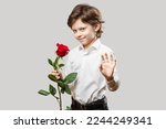 Little Boy Wearing a White Shirt Holding a Single Red Rose Flower Smiling and Waving with his Hand. Romantic or Saint Valentines Day Concept