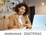 Confident African American young woman with stylish afro hairstyle, smart student studying, taking notes on notepad watching training courses on laptop. Online business or education concept