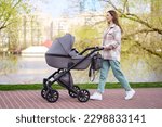 Portrait of beautiful smiling young mother pushing stroller with little baby walking in spring park. Motherhood, healthy lifestyle concept