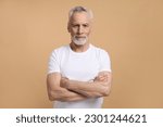 Caucasian confident handsome imposing retired senior man 60 years old, smiling, looking confidently at camera, posing with arms folded isolated on beige background. Mature people and lifestyle concept
