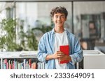 Portrait of smiling smart curly haired teenage boy holding book looking at camera. Back to school, Education concept