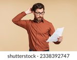 Small photo of Portrait of handsome pensive middle aged student man wearing eyeglasses holding documents, reading information isolated on beige background. Frustrated businessman, freelancer missed deadline