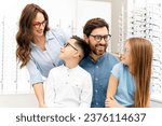 Young beautiful smiling family choosing glasses in modern optical store looking each other. Health care, Vision concept