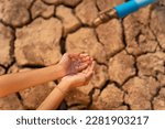 Hand of little girl wating for a drip of water from a faucet at dry ground. Water scarcity and crisis concept. 
