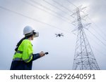 A female electrical engineer flying drone survey area of high voltage pylon with vr goggles at high voltage power plant pylon to plan electric power generation at high voltage pylon.