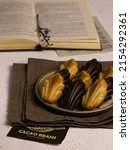 Small photo of Madeleine cookies with chocolate glaze on the ceramic plete, brown linen cloth, opened book on the background