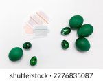 Small photo of Dyestuff, colorant in paper bag, package for coloring Easter eggs on white background, green painted chicken, quail eggs lying around. Top view, flatly horizontal plane. High quality photo