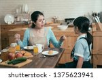 Small photo of lazy sleepy little girl wake up late for school sitting at kitchen table with breakfast at home. frowning angry mom loudly nag at daughter bad habit in early morning. unhappy asian mother worried.