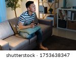 Small photo of Young asian chinese man addicted to video gaming at dark home. concentrated handsome guy in casual wear stay up late house living room. male sitting on sofa holding joystick remote in evening.