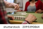 Small photo of closeup with selective focus of a hand tapping on the table while waiting for his turn at gambling table. asian traditional strategy game concept. words on mahjong tile translation: east