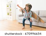 Small photo of smiling sweet female children wearing astronaut costume making ready to fly gesture standing on living room wooden floor at home.