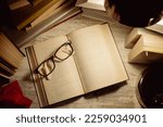 top view open book with glasses on top surrounded by stacked books and the light from a lamp