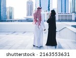 Back view of Arab family or business work colleagues pointing towards city skyline wearing traditional abaya and dress. Muslim Saudi or Emirati couple or team working together