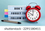 Small photo of Text DONT FORGET TO FOLLOW UP written on the lightbox with alarm clock and colorfull stickers on blue background