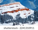 Red Rock Butte in winter snow in the Shoshone National Forest with mountains in the background and evergreen trees in the foreground
