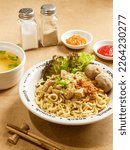 Small photo of a bowl of chicken noodles with an additional topping of 2 meatballs served on the table with an additional bowl of soup, sauce, chili sauce, pepper and salt as a complement. served eith chopstick.