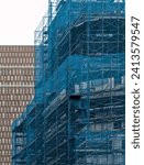 Small photo of building under construction covered in blue mesh tarp protective wrap (safety debris netting during demolition work) scaffolding high rise commercial architecture