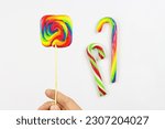 Small photo of Multicolored square lollipop, sweet candy in rainbow colors after expiry date. Lollypop on white background with other colorful lollipops blurred behind, ugly food