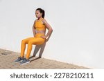 Small photo of Fit woman doing squat exercise against a wall