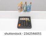 Small photo of Banknotes arranged in a roll of 3 denominations of 50 zloty 100 zloty and 200 zloty next to which lies a wooden Bank sign on a calculator. The concept of spending during a crisis of inflation and rece