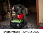 Small photo of Man wear in military jacket pour gasoline from canister in portable mobile backup standby generator.