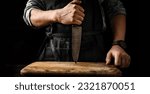 Small photo of Chief man in apron stubs knife blade to wooden board at kitchen. Restaurant professional with culinary tool